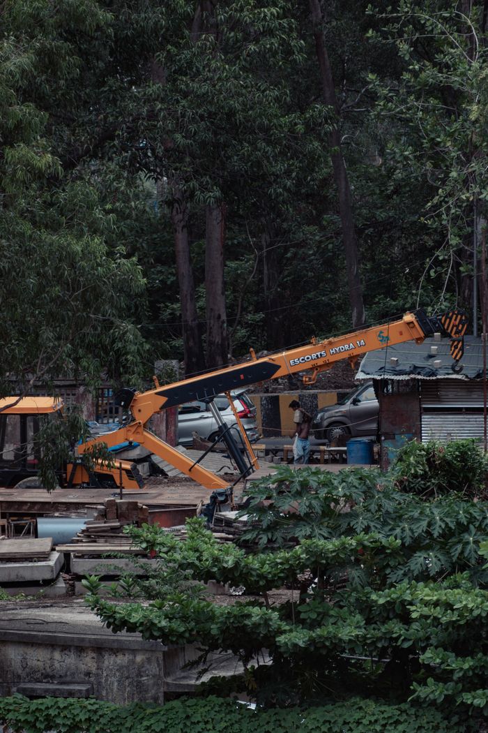 An excavator at a construction site surrounded by dense forest, depicting rural development.